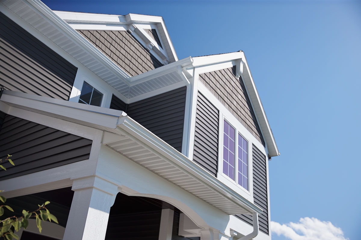 Modern home exterior featuring dark vinyl siding, crisp white trim, and precision-finished gutters under clear blue sky